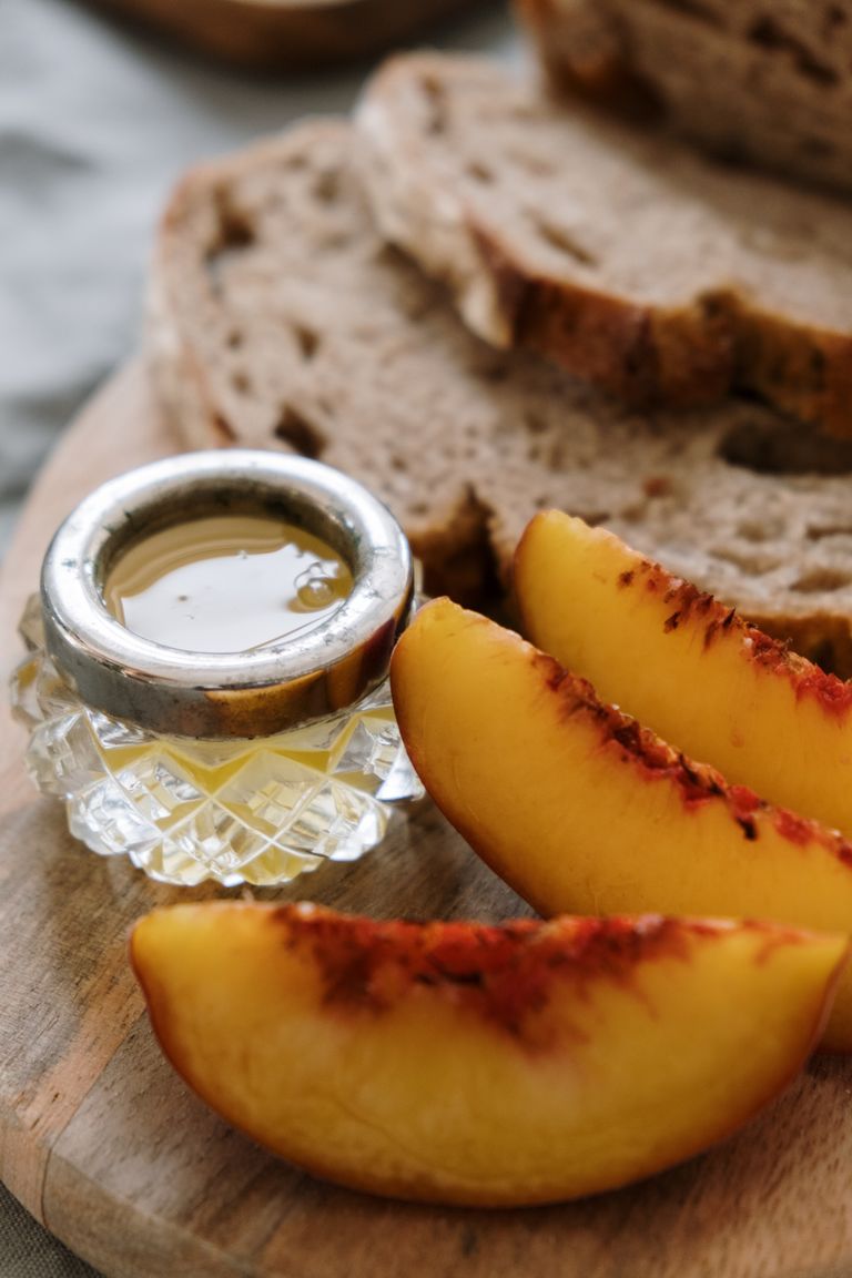 Slices of fresh peach with honey and rustic bread on a wooden board.
