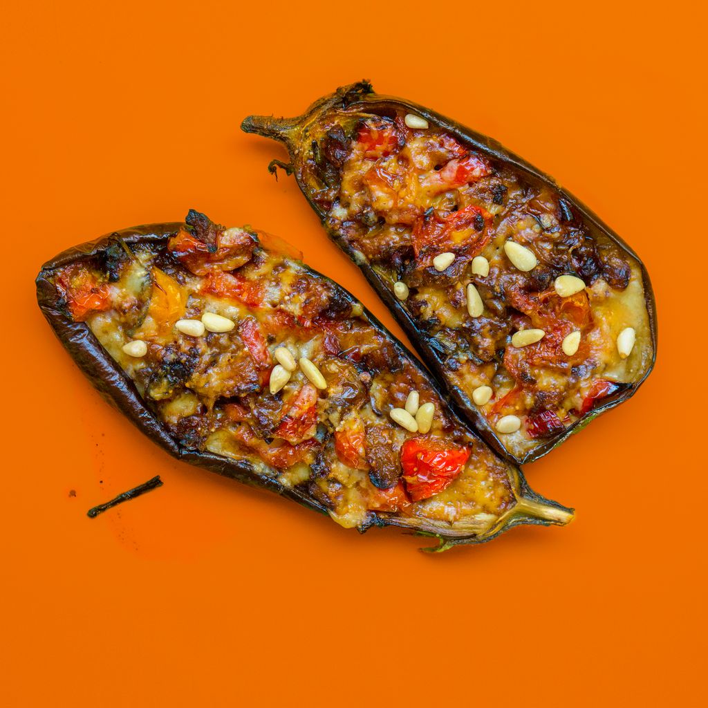 Tasty baked eggplants stuffed with vegetables and pine nuts on an orange background.