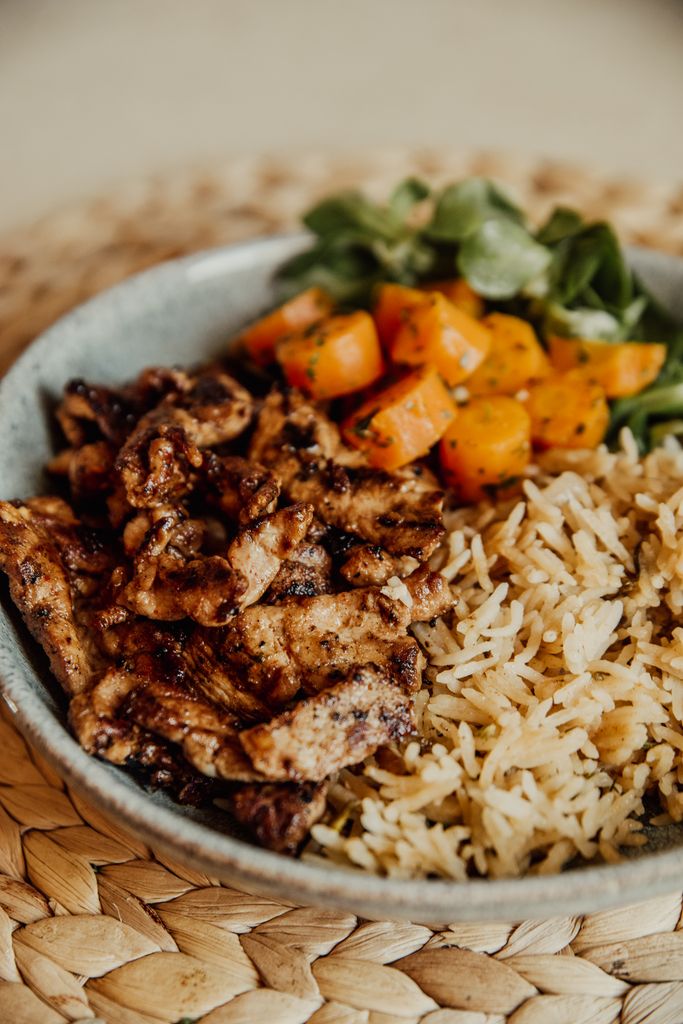 Tasty grilled chicken with rice and colorful vegetables served in a bowl, perfect for a healthy meal.