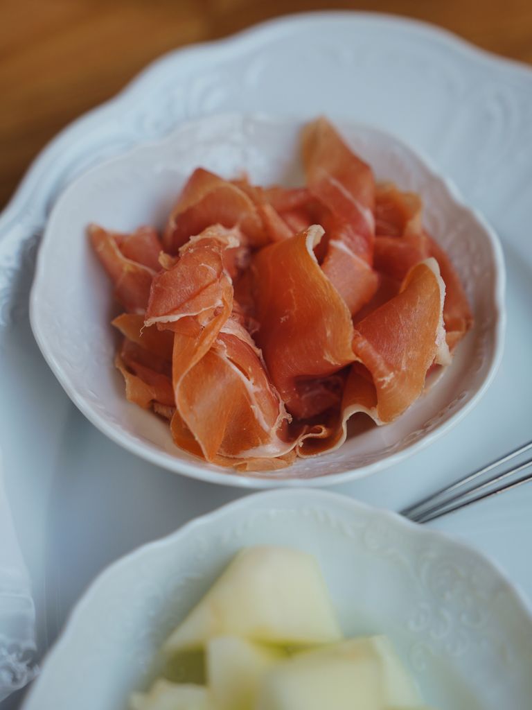 Thinly sliced prosciutto in a white bowl on an elegant plate setting.