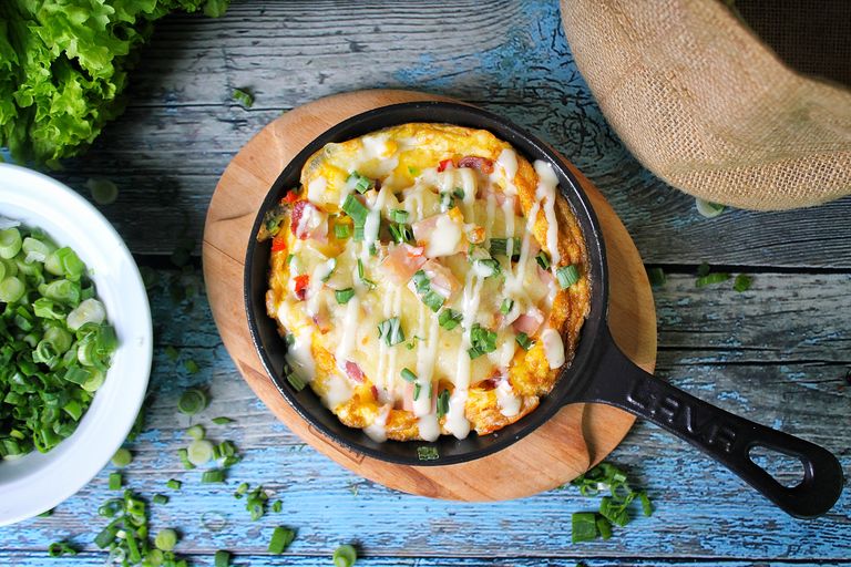 Top view of a baked casserole in a skillet with green onions on a rustic wooden background.