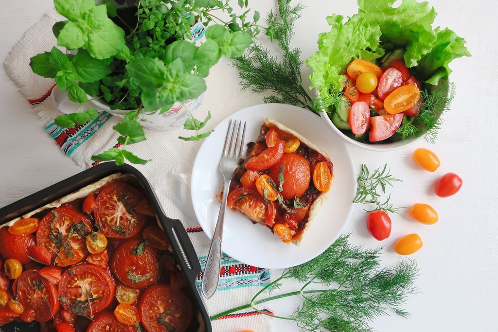 Top view of a vibrant tomato tart paired perfectly with a fresh salad and herbs.