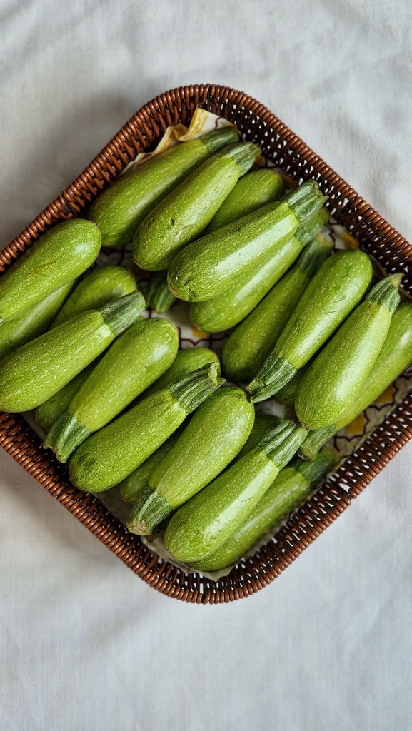Top view of fresh green zucchinis in a decorative wicker basket over a neutral background.