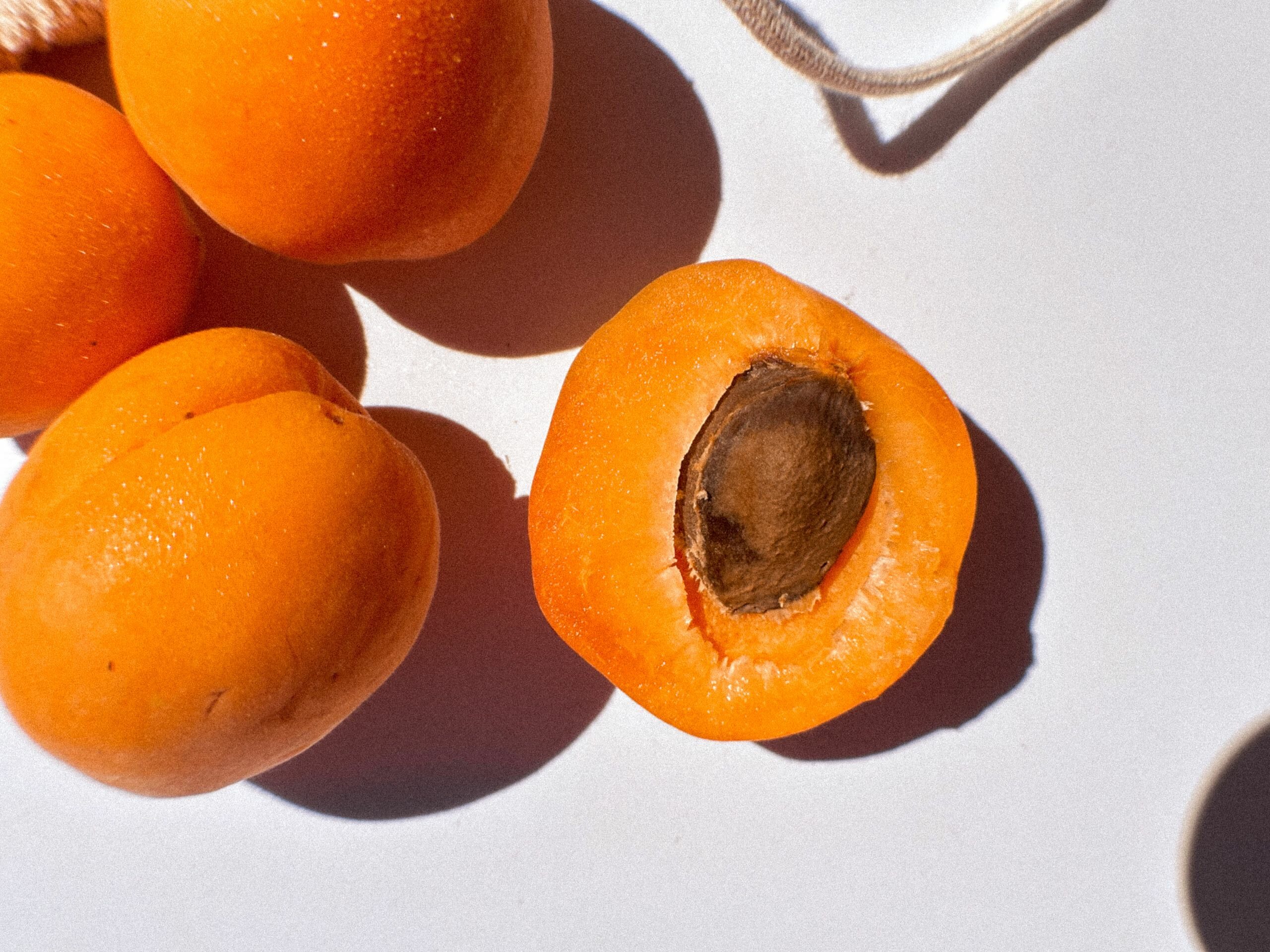 Top view of fresh organic apricots with one cut open, showcasing a ripe seed against a white background.