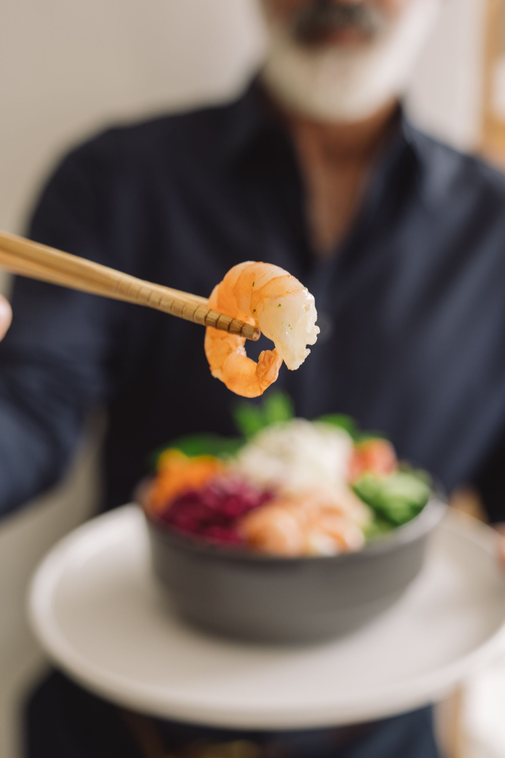 A delicious shrimp held by chopsticks over a vibrant rice bowl with mixed vegetables. Ideal for food photography.