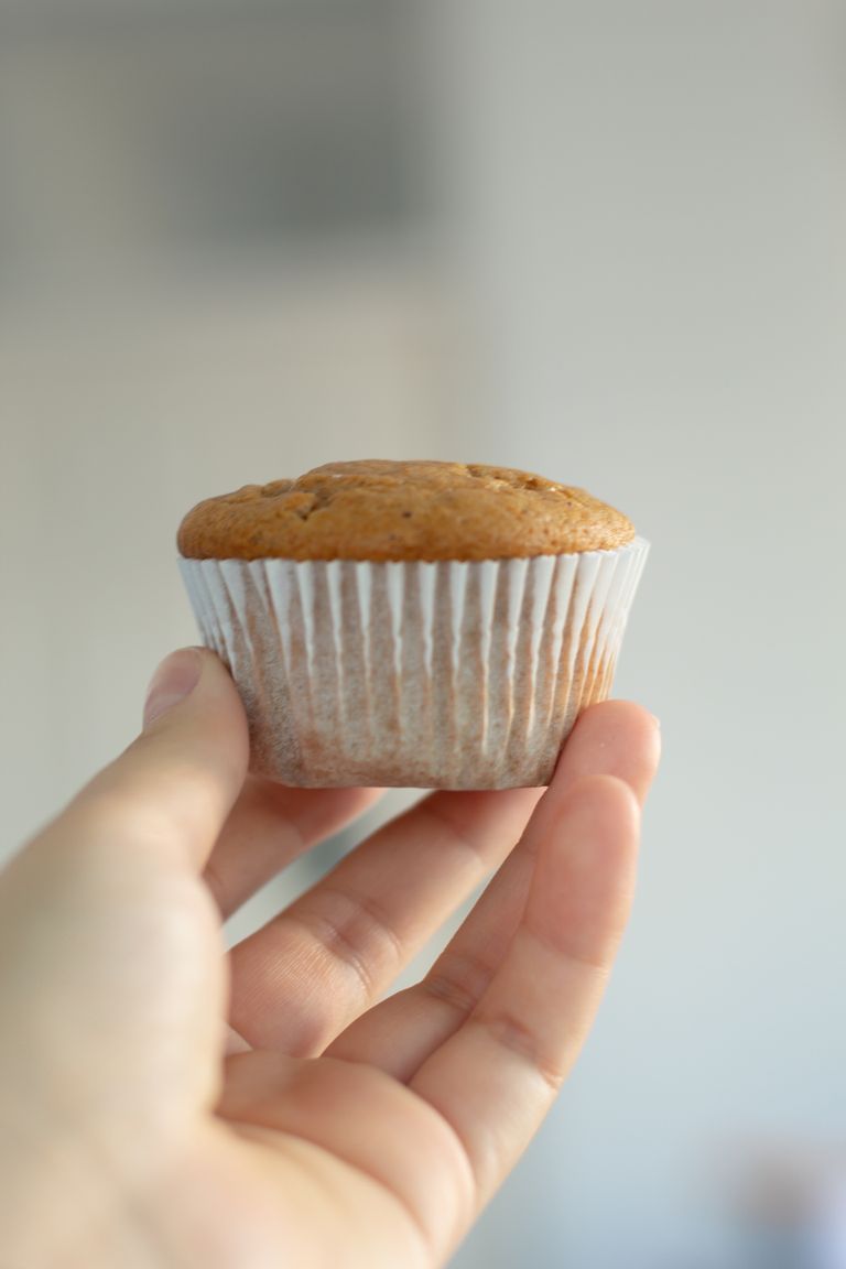 A hand holds a fresh muffin against a soft blurred background, showcasing simplicity and food delight.