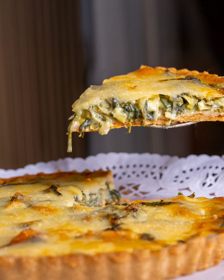 Close-up of a fresh spinach quiche slice being served on a doily.