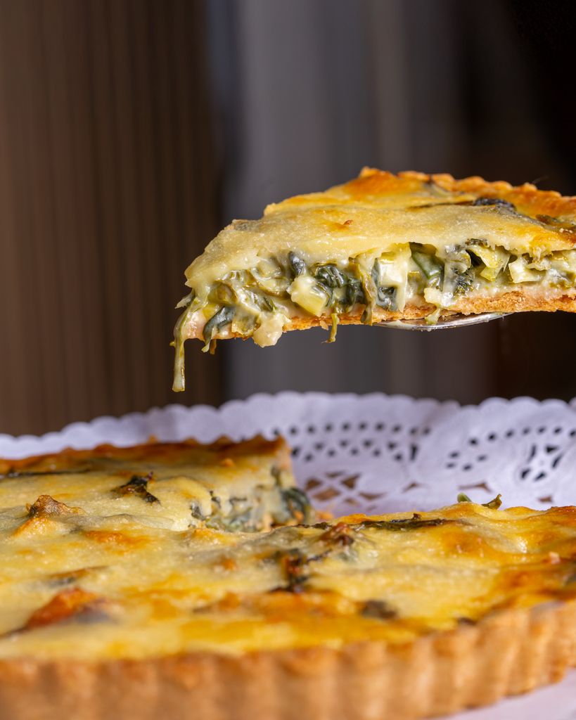 Close-up of a fresh spinach quiche slice being served on a doily.