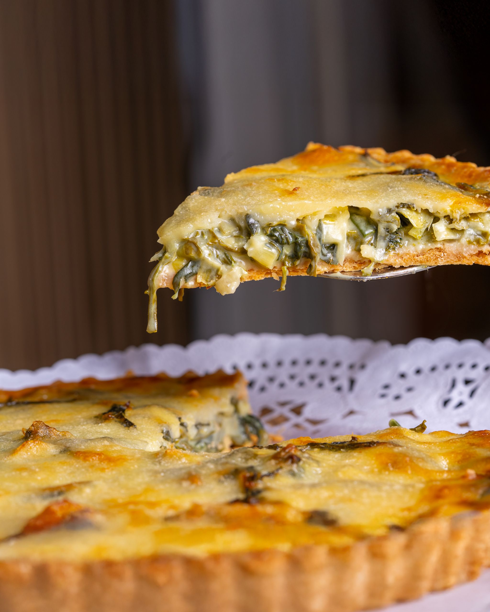 Close-up of a fresh spinach quiche slice being served on a doily.
