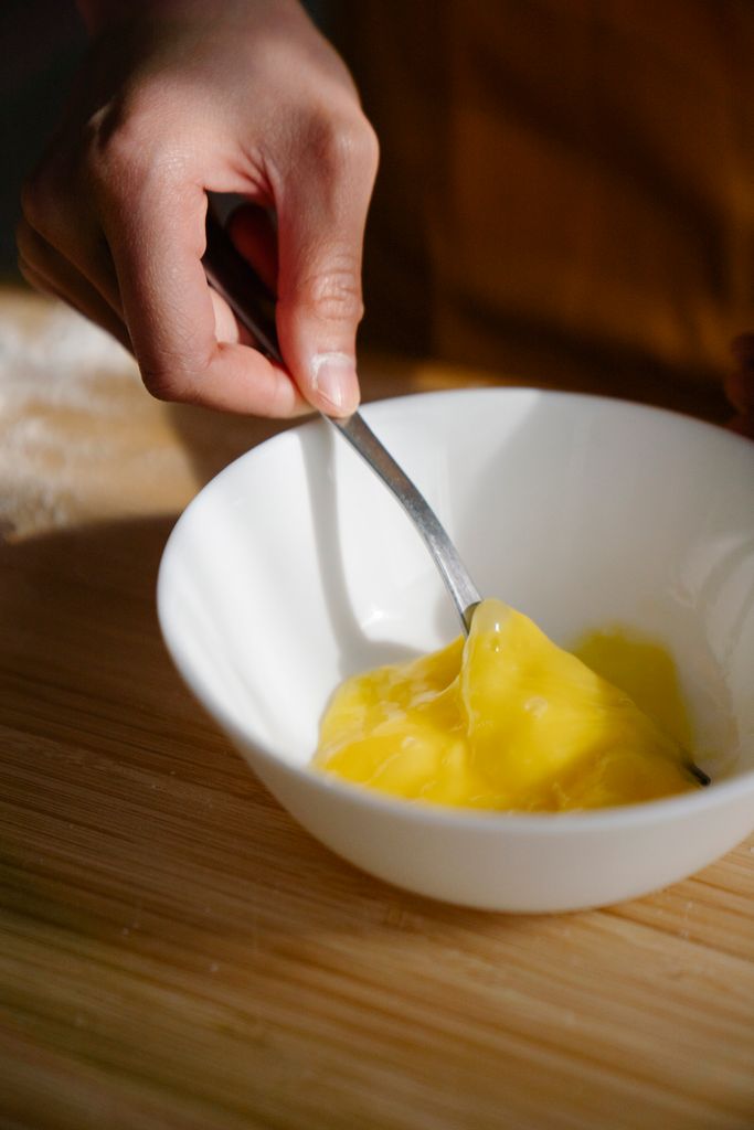 Close-up of a hand mixing a raw egg yolk in a white bowl with a fork.