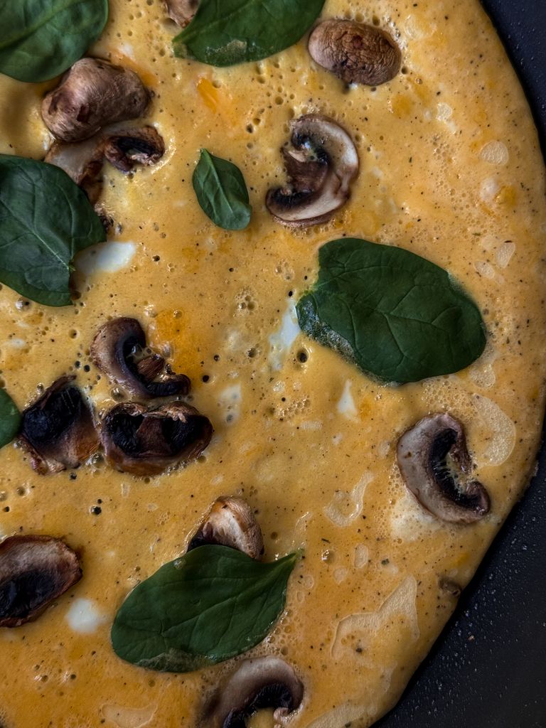 Close-up of a mushroom and spinach omelette in a frying pan, showcasing vibrant ingredients.