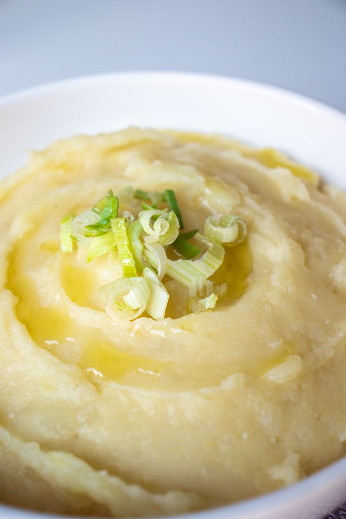 Close-up of creamy mashed potatoes topped with fresh green onions in a white bowl.