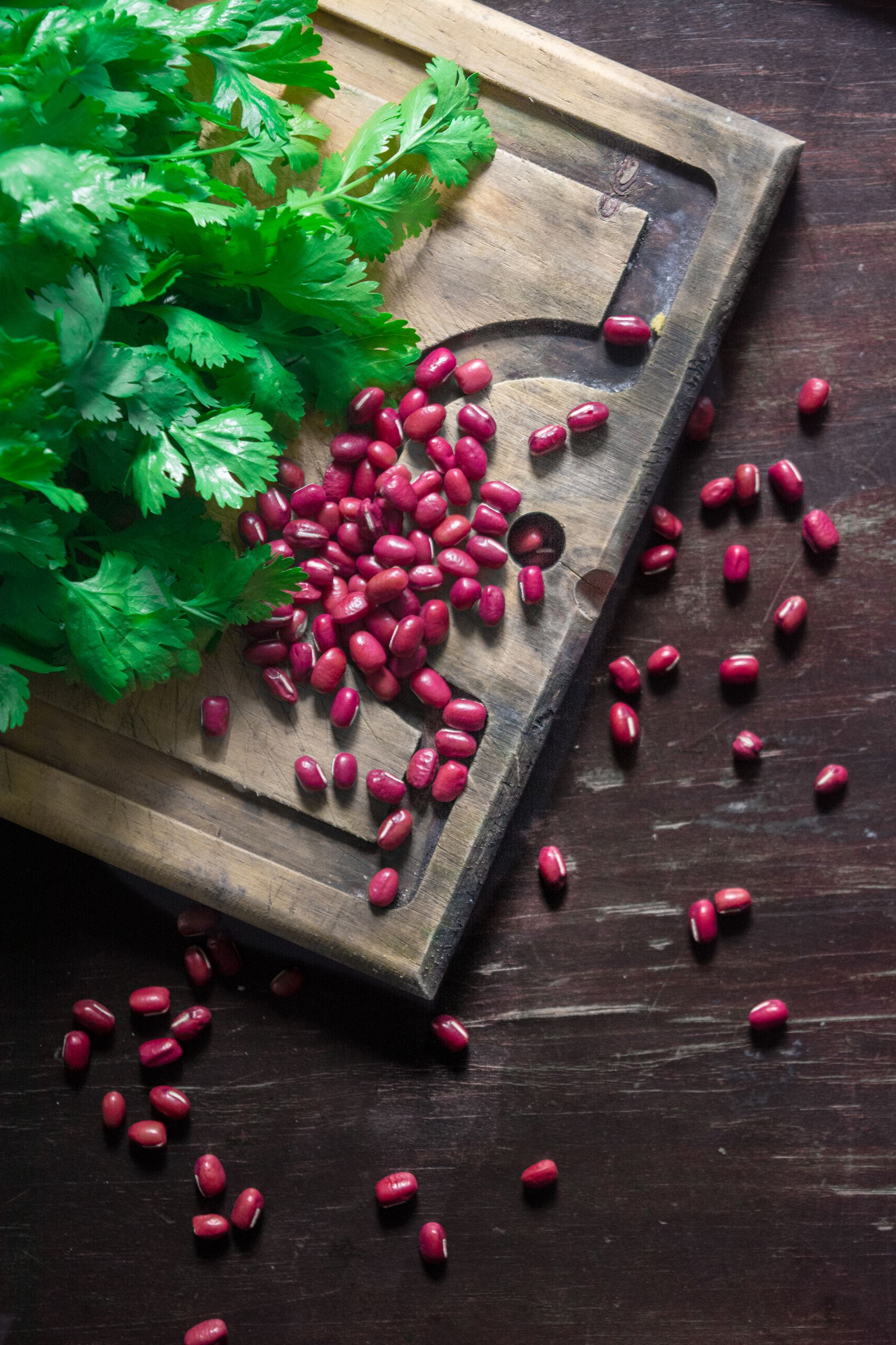 Close-up of fresh cilantro and red beans on a rustic chopping board, emphasizing organic food preparation.
