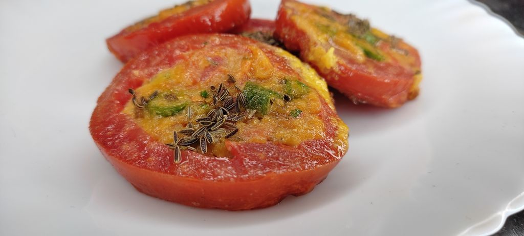Delicious close-up of tomato slices stuffed with herbs and spices on a white plate.