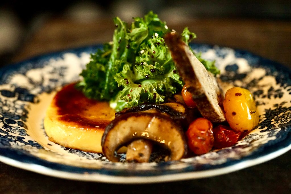 Delicious gourmet dish featuring mushrooms, sauteed greens, polenta, and cherry tomatoes served on a vintage plate.