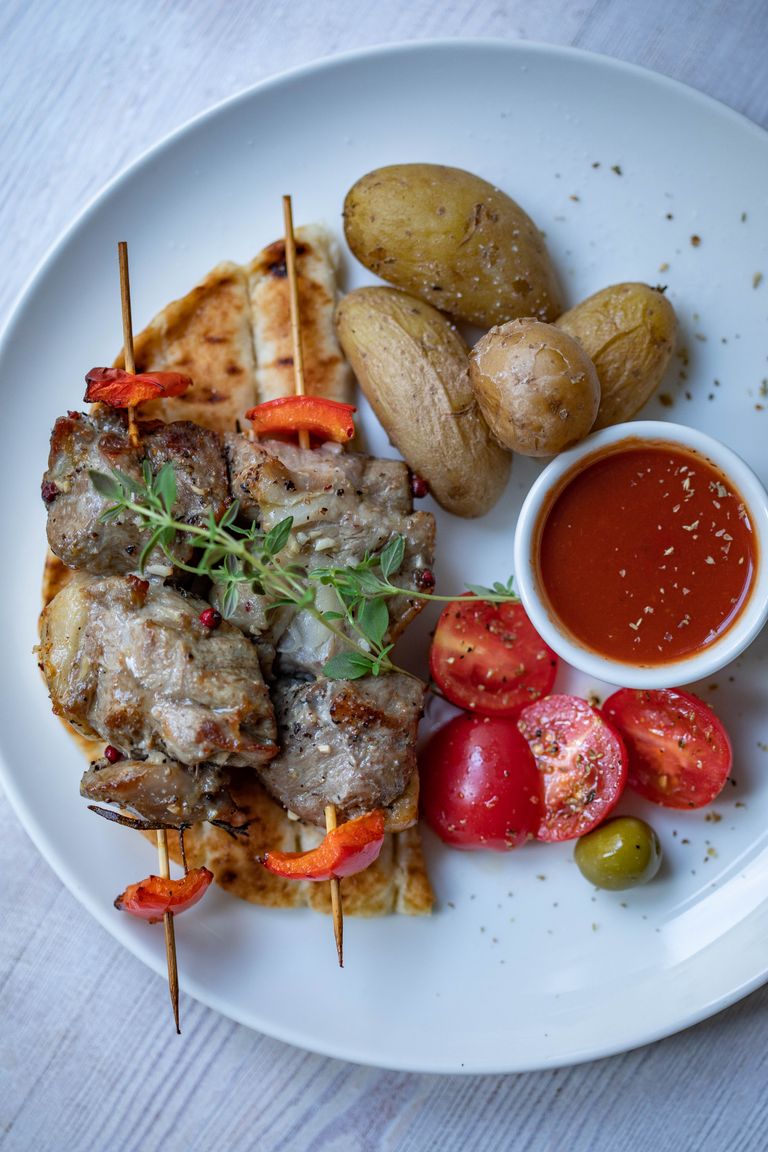 Delicious grilled skewers with potatoes, fresh vegetables, and sauce on a plate, perfect meal concept.