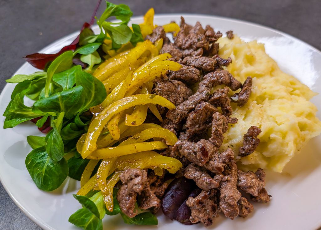 Delicious plate of beef stir-fry with mashed potatoes, yellow bell peppers, and greens.