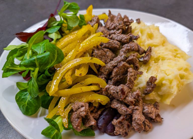 Delicious plate of beef stir-fry with mashed potatoes, yellow bell peppers, and greens.