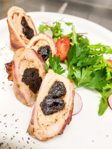 Delicious rolled chicken with prunes and fresh salad garnish, gourmet plating.