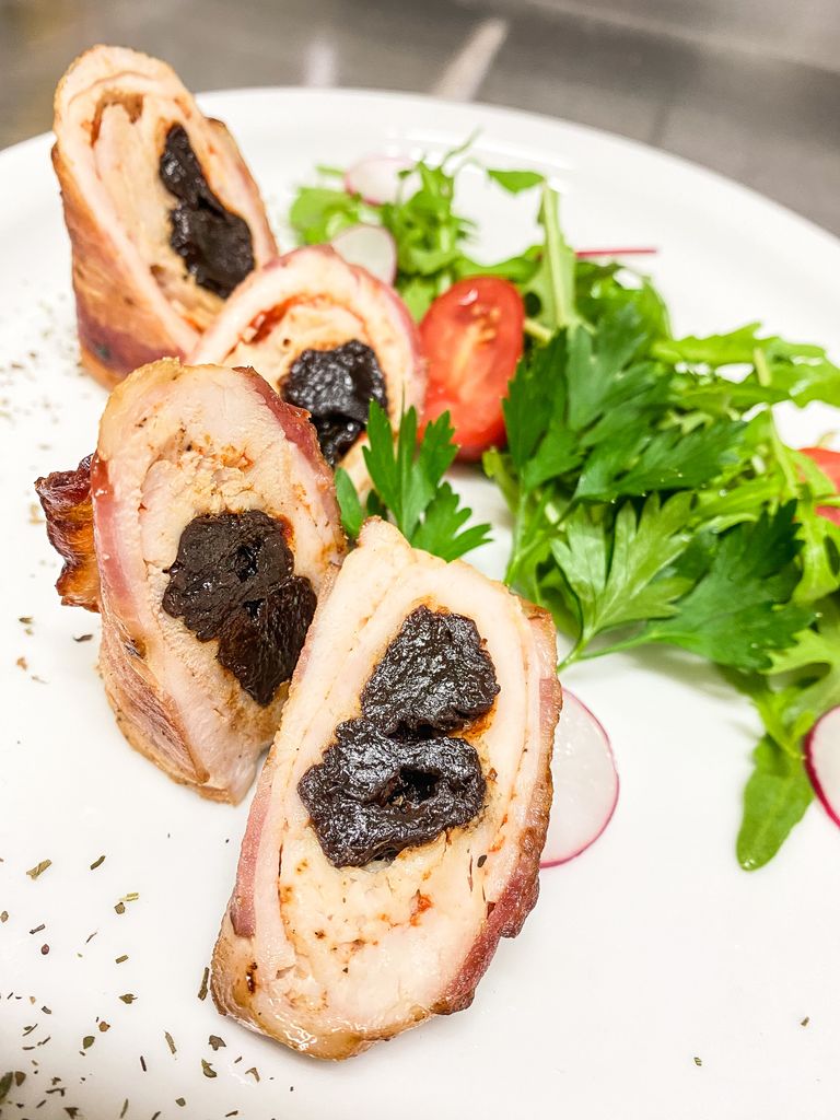 Delicious rolled chicken with prunes and fresh salad garnish, gourmet plating.