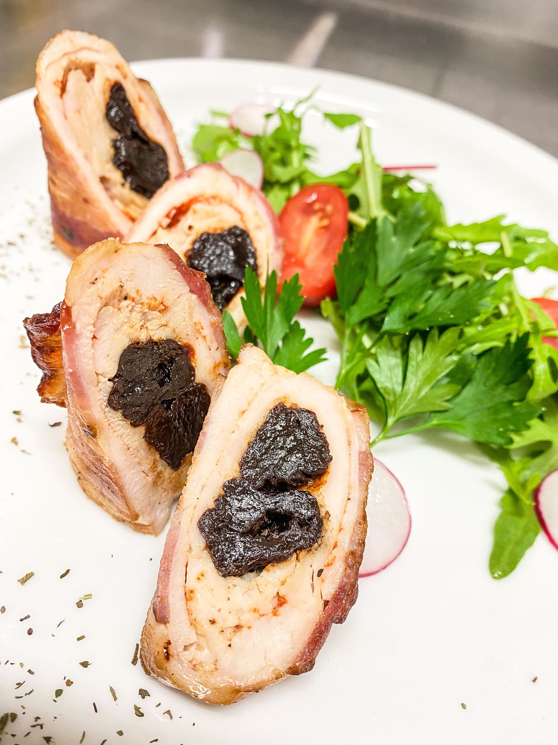 Delicious rolled chicken with prunes and fresh salad garnish, gourmet plating.