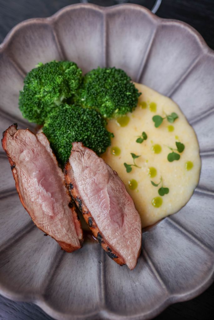 Elegant presentation of sliced duck breast, broccoli, and creamy polenta with herb oil.