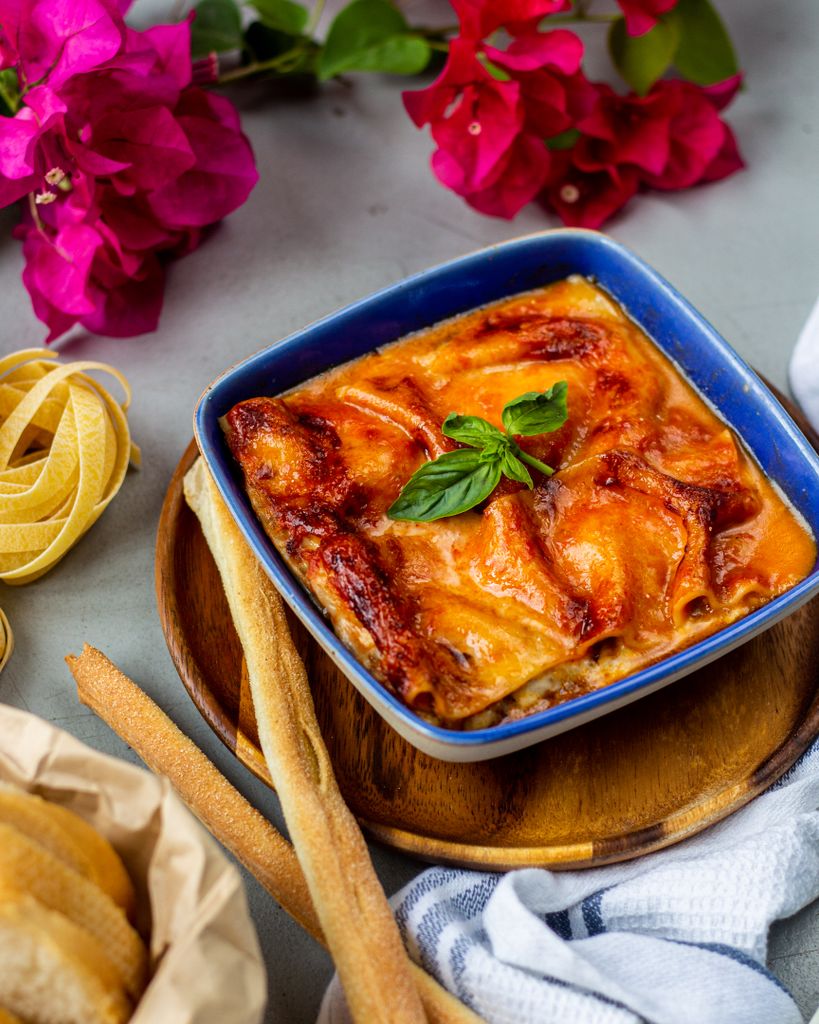 Enjoy the rich flavors of homemade Italian lasagne served in a blue dish with a basil garnish.