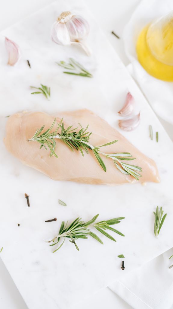 High-angle shot of raw chicken breast with rosemary and garlic on a marble slab.