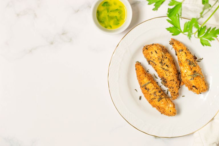 Tasty fried chicken tenders with herbs on a white plate and marble background.