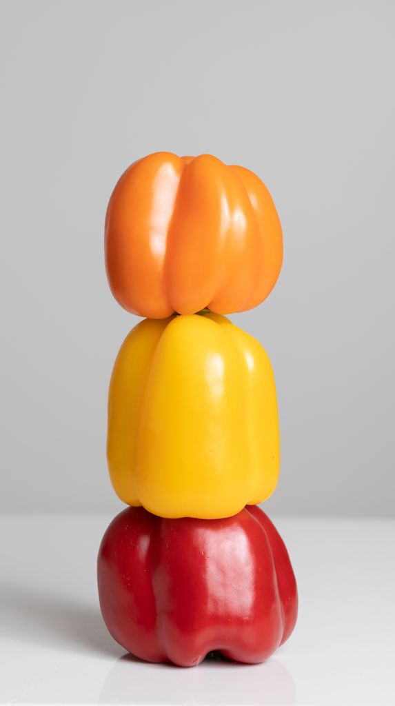 Three colorful bell peppers stacked vertically creating a vibrant contrast against a gray background.