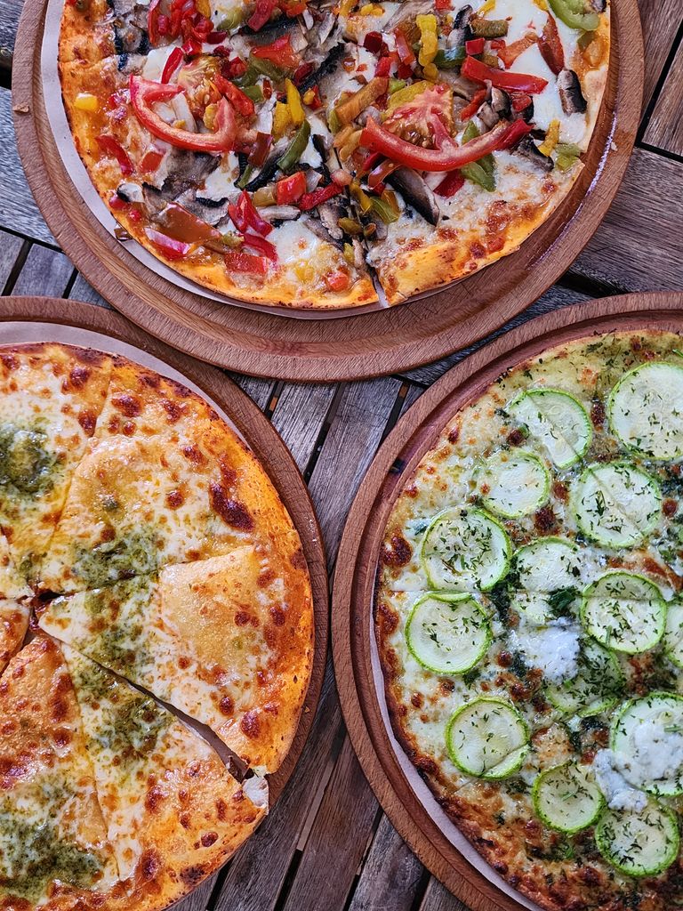Three pizzas with diverse toppings served on wooden plates, showcasing food photography appeal.
