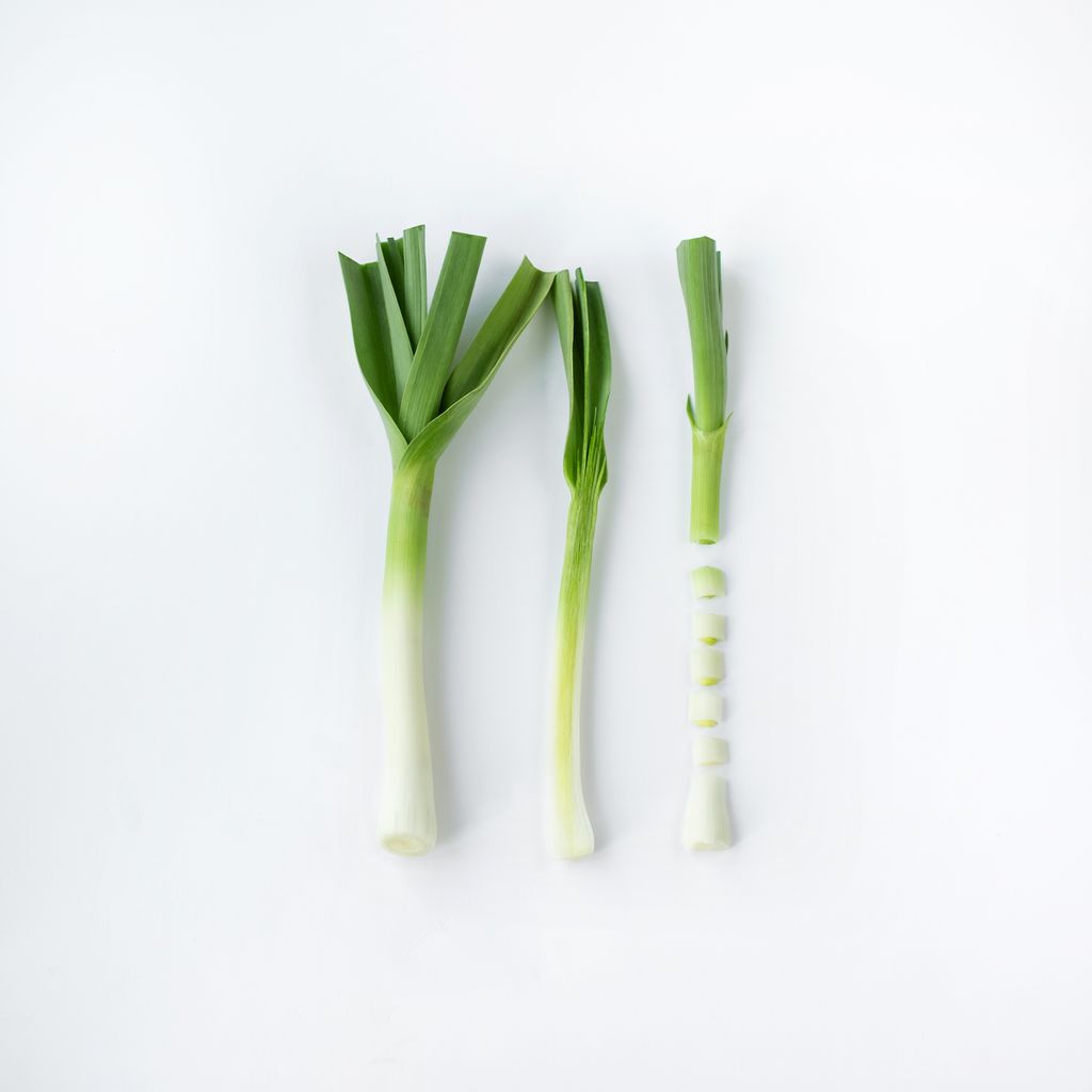 Three stages of leek preparation on a white background - whole, trimmed, and sliced.