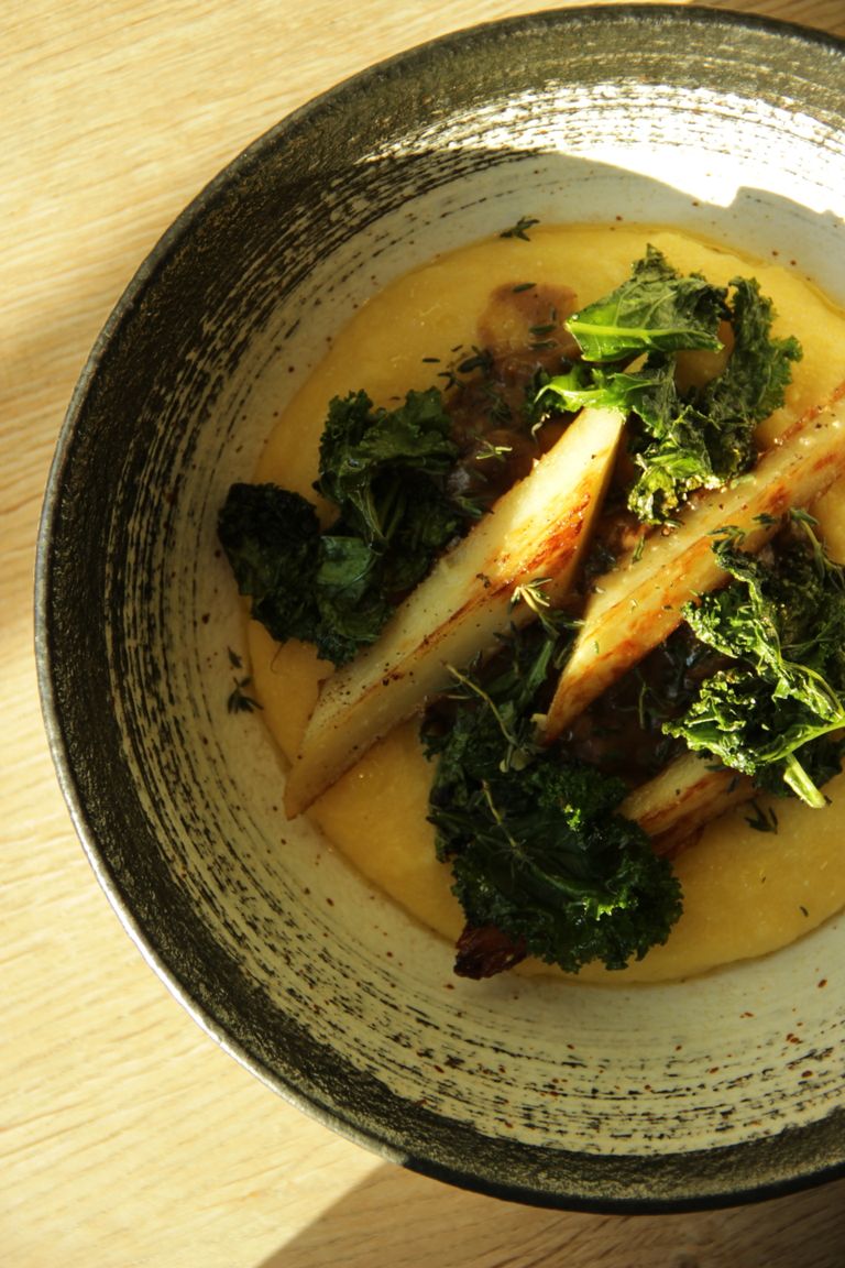 Top view of a gourmet dish featuring roasted vegetables and kale on creamy polenta.