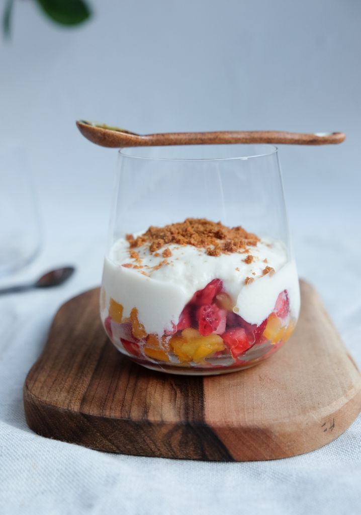 A vibrant fruit and yogurt dessert with granola in a clear glass on wooden board.