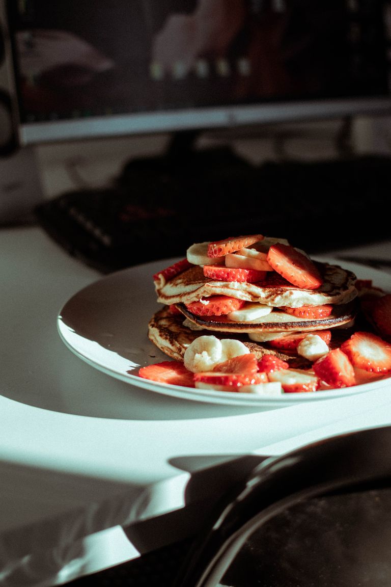 Stack of homemade pancakes with strawberries and bananas in a sunlit room.