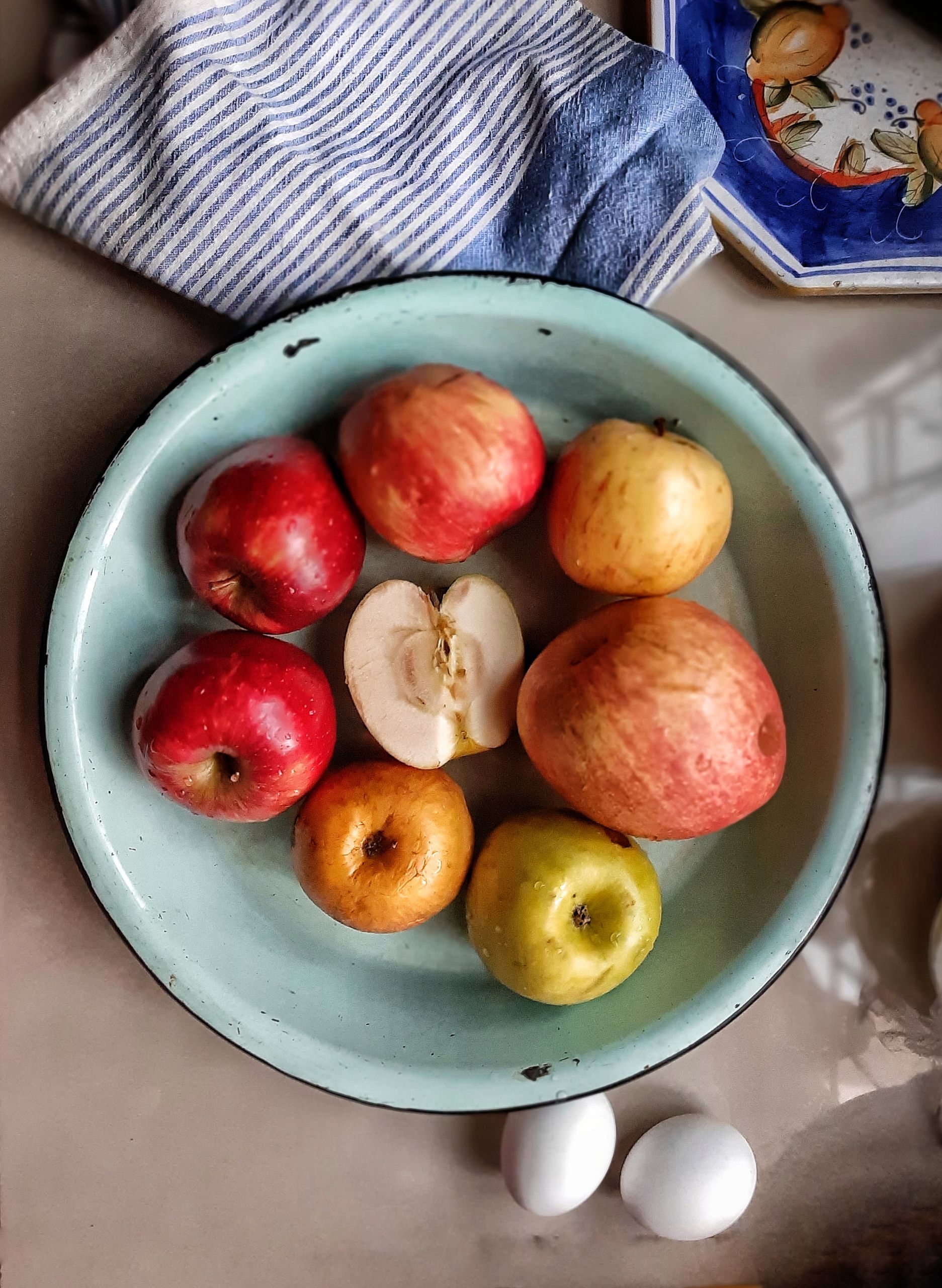 Vibrant apples and eggs arranged in a rustic enamel bowl, ideal for food photography and culinary themes.